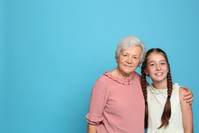Photo of Cute girl and her grandmother on light blue background. Space for text