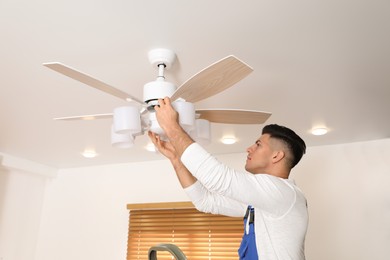 Electrician repairing ceiling fan with lamps indoors