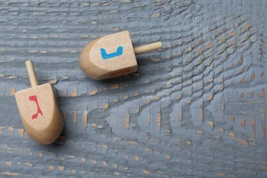 Hanukkah traditional dreidels with letters Nun and Gimel on grey wooden table, flat lay. Space for text