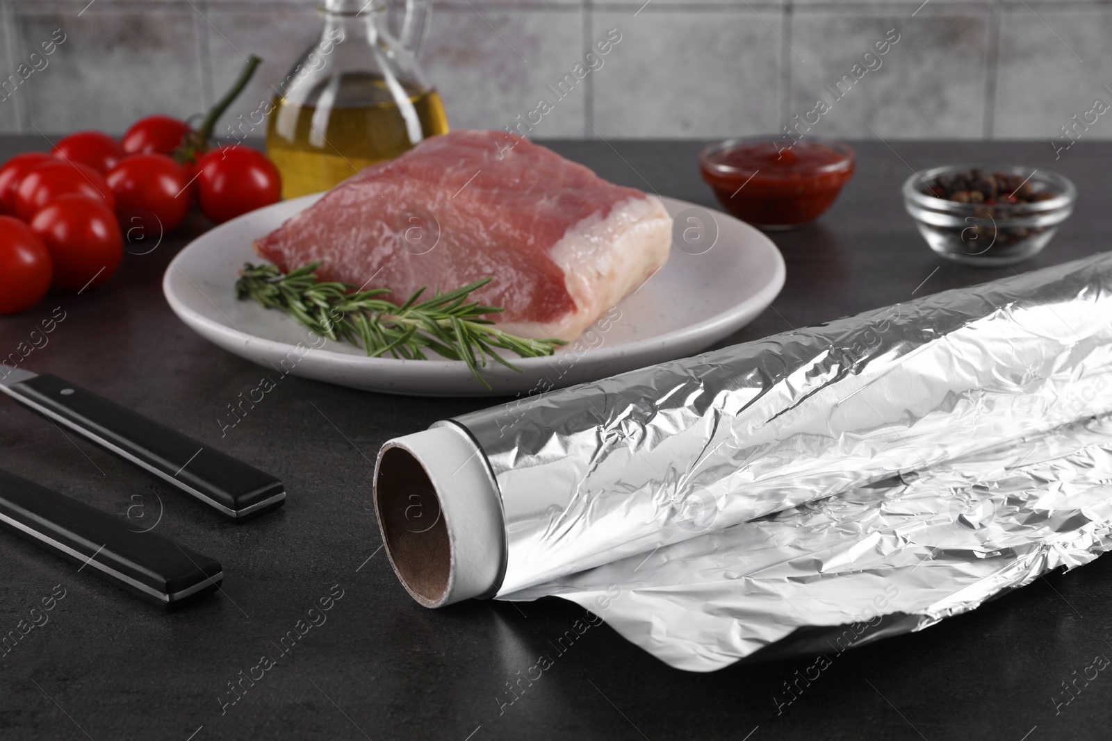 Photo of Aluminum foil, products and raw meat on dark table, closeup