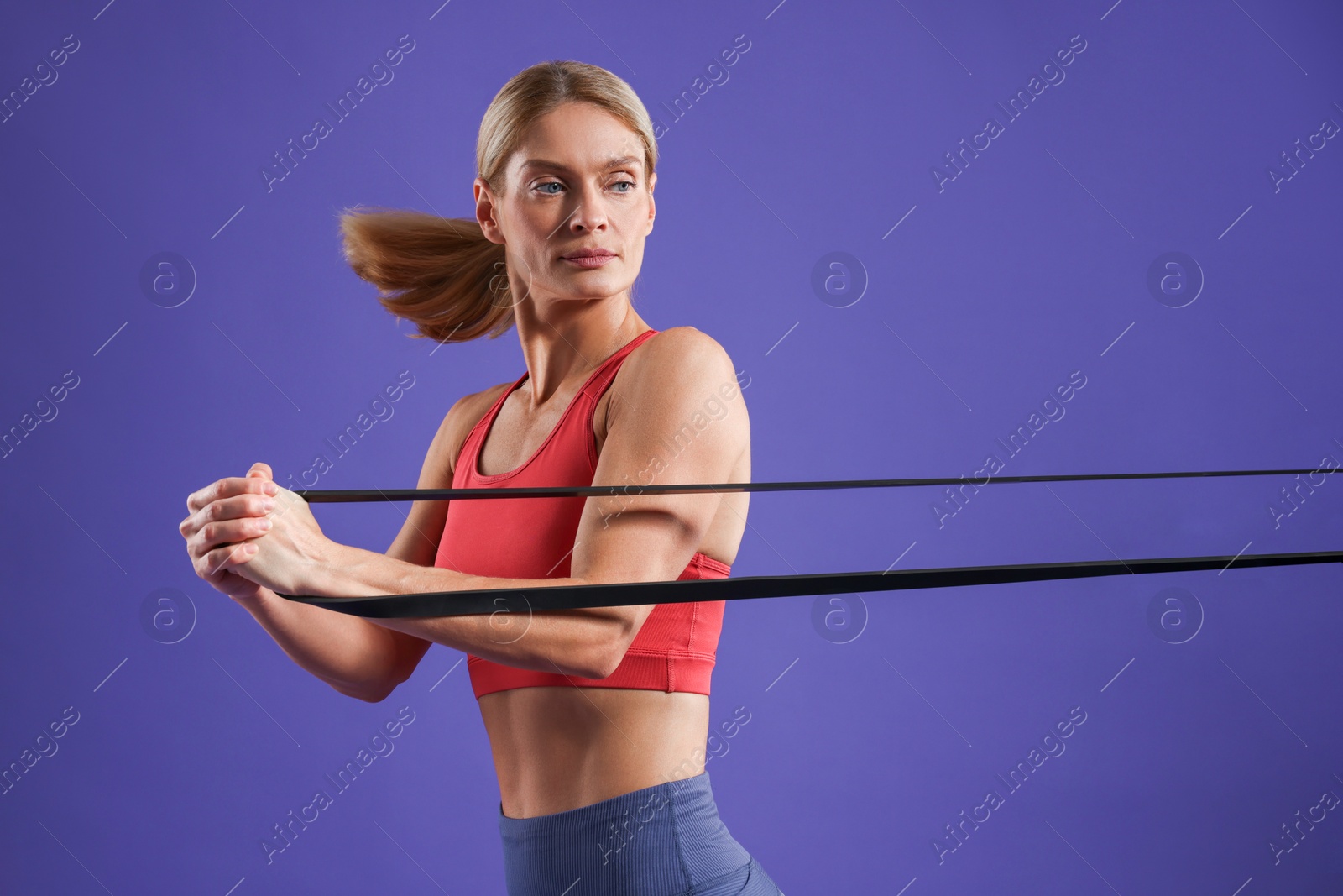 Photo of Athletic woman exercising with elastic resistance band on purple background