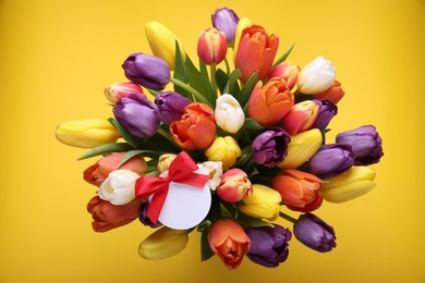 Photo of Bouquet of beautiful colorful tulips with blank card on yellow background, top view. Birthday celebration