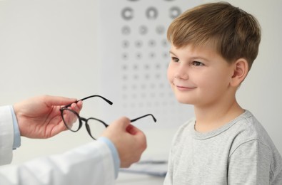 Vision testing. Ophthalmologist giving glasses to little boy indoors