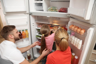 Young family choosing food in refrigerator at home