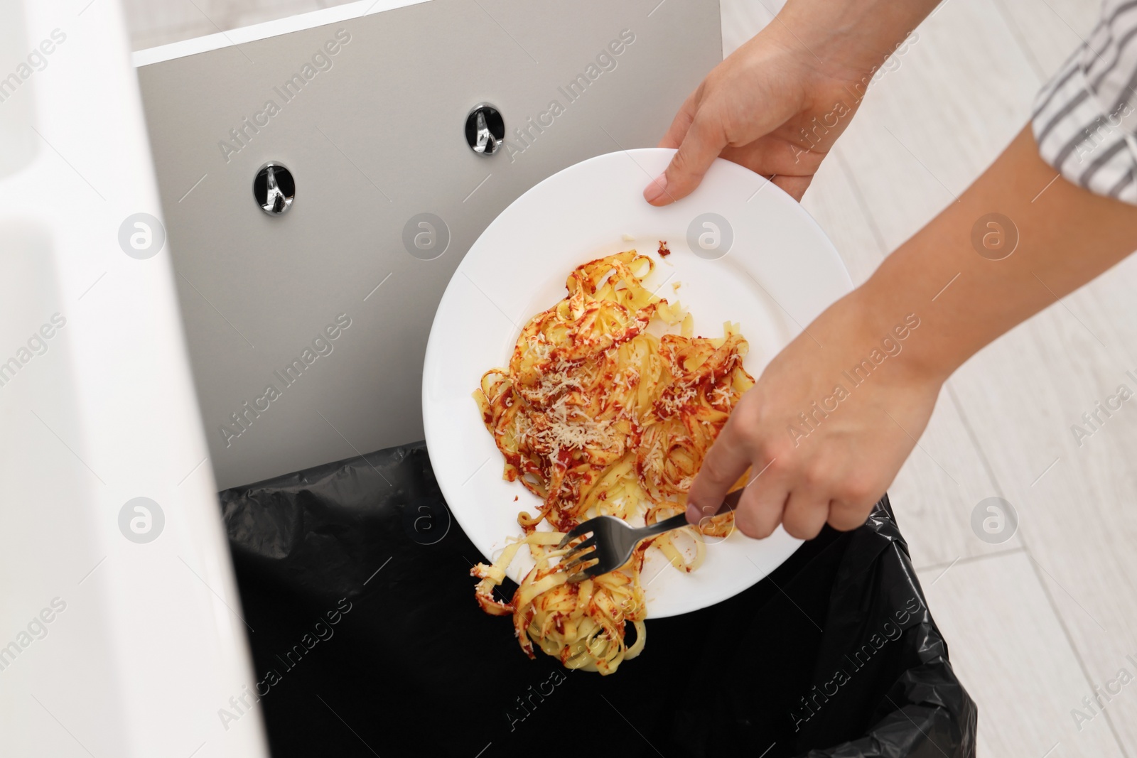 Photo of Woman throwing pasta into bin indoors, closeup