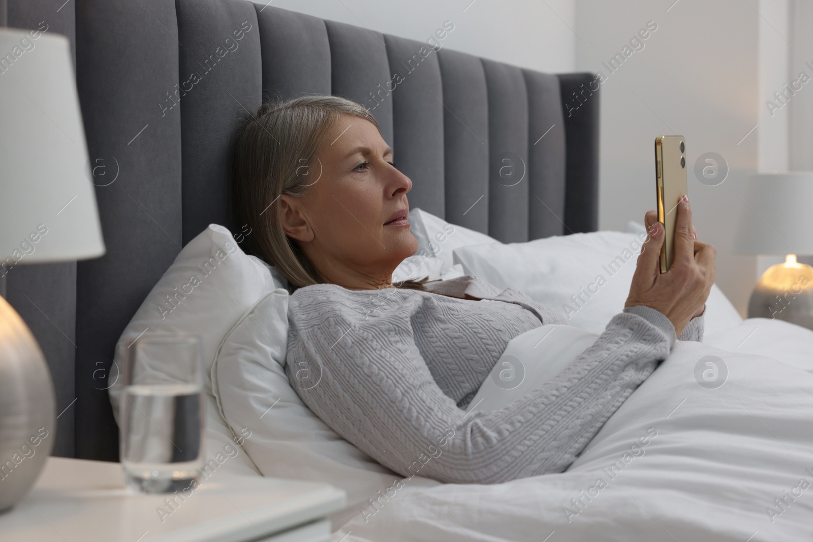 Photo of Menopause. Sleepless woman using smartphone in bed indoors