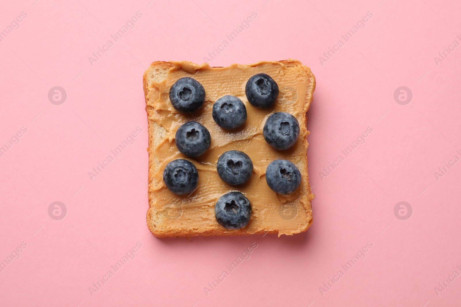 Photo of Tasty peanut butter sandwich with fresh blueberries on pink background, top view