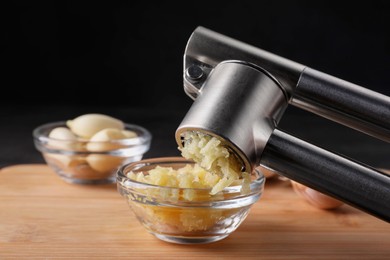 Photo of Crushing garlic with press into bowl at wooden table, closeup