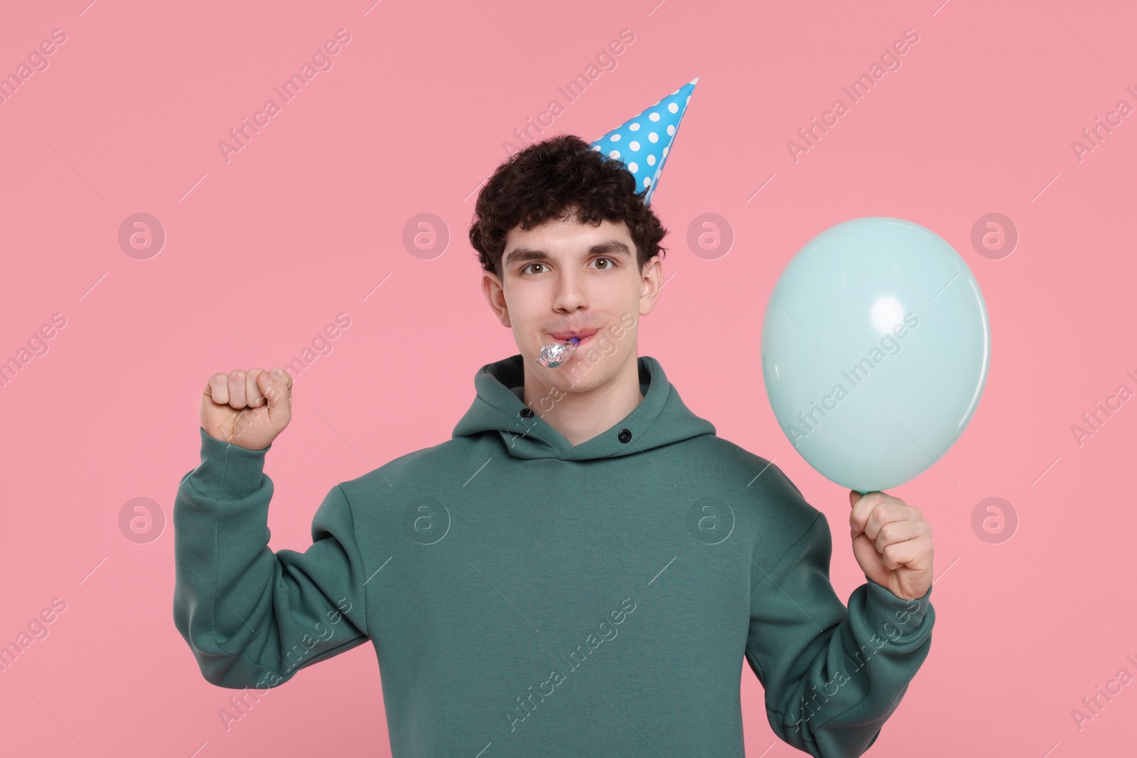 Photo of Young man in party hat with blower and balloon on pink background