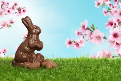 Image of Chocolate bunny and eggs on green grass outdoors, space for text. Easter celebration