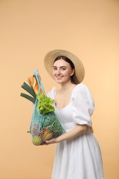 Woman with string bag of fresh vegetables and baguette on beige background