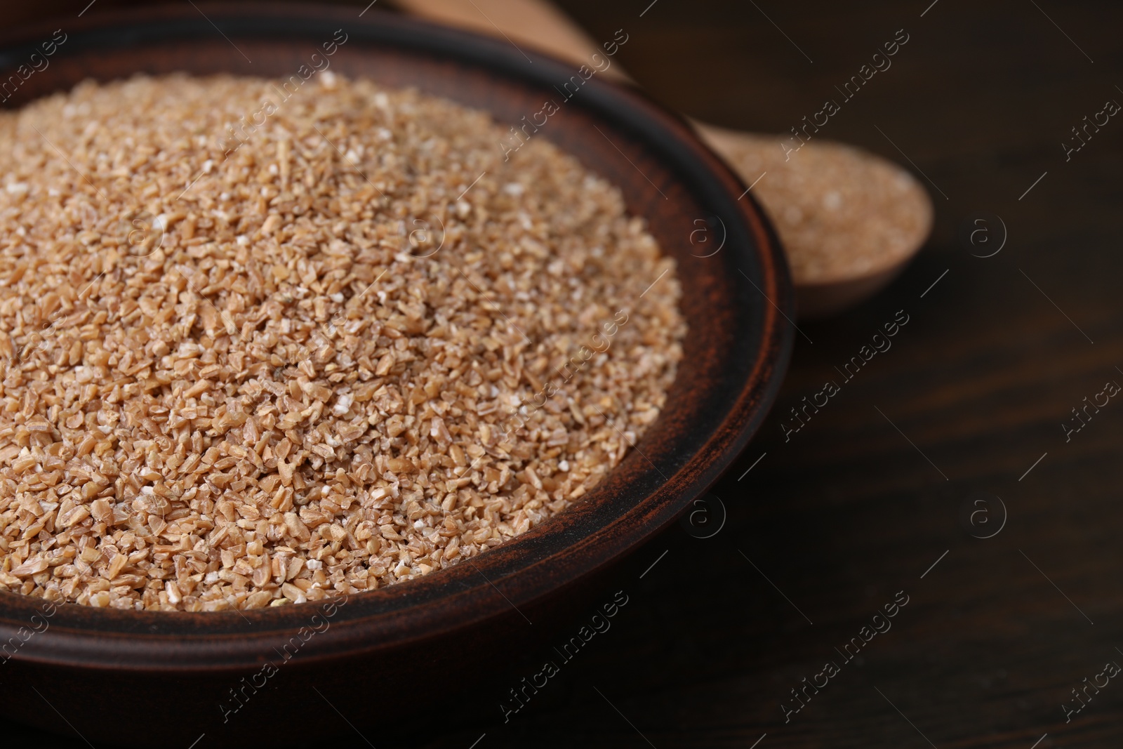 Photo of Dry wheat groats in bowl on wooden table, closeup