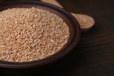 Dry wheat groats in bowl on wooden table, closeup