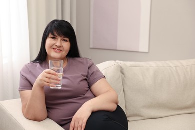 Photo of Beautiful overweight woman with glass of water on sofa at home