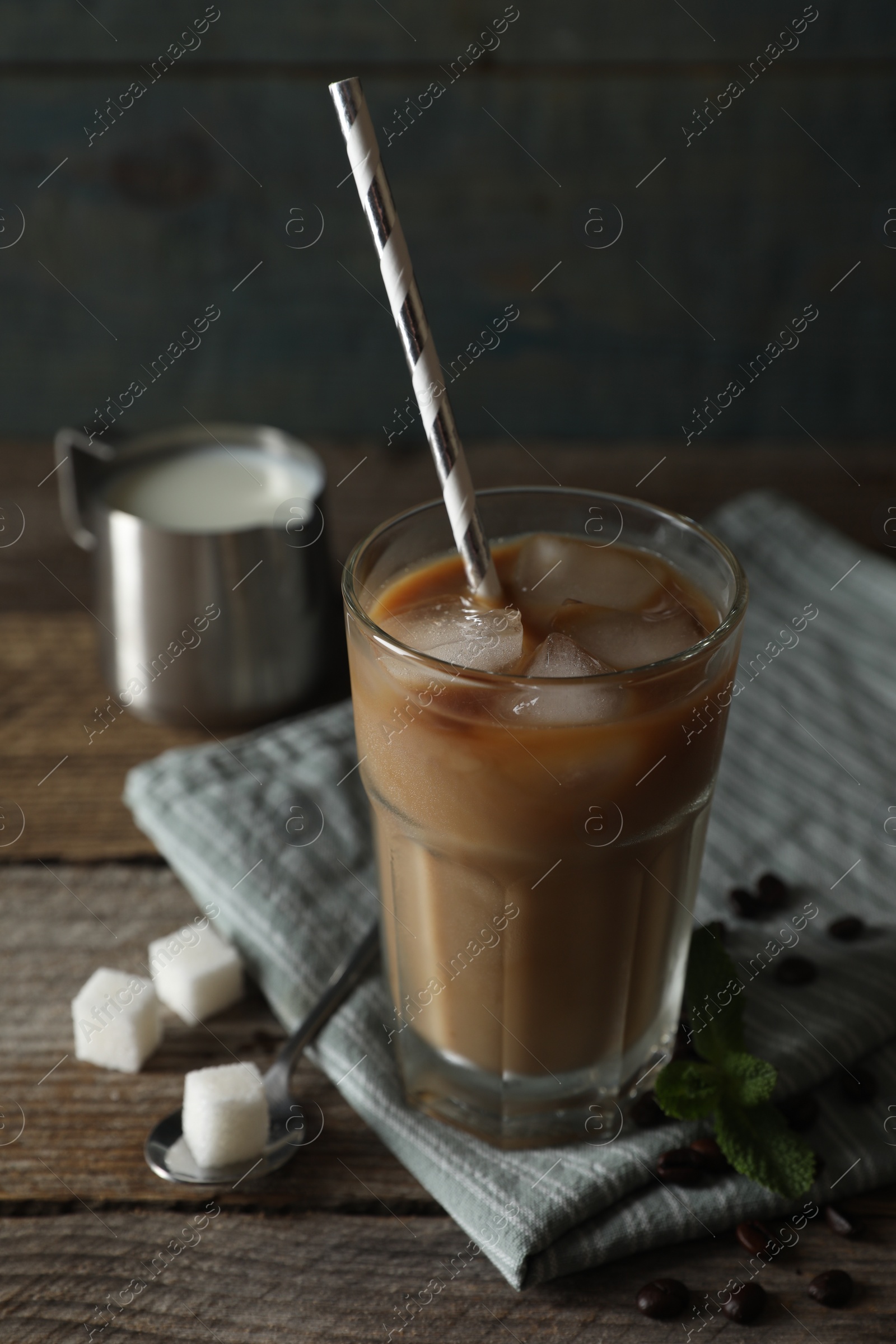 Photo of Glass of delicious iced coffee with milk, beans and sugar cubes on wooden table