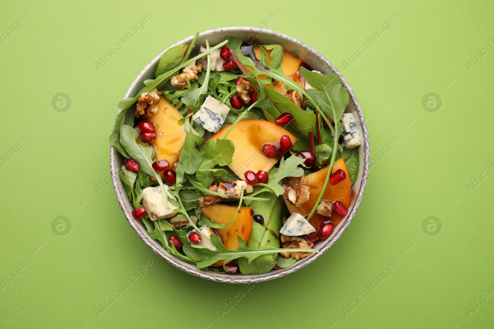 Photo of Tasty salad with persimmon, blue cheese, pomegranate and walnuts served on light green background, top view