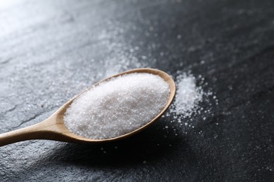 Photo of Organic white salt in spoon on black table, closeup. Space for text