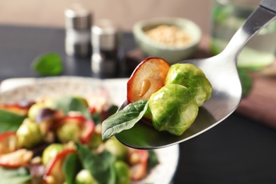 Photo of Spoon with tasty Brussels sprouts salad over table, closeup