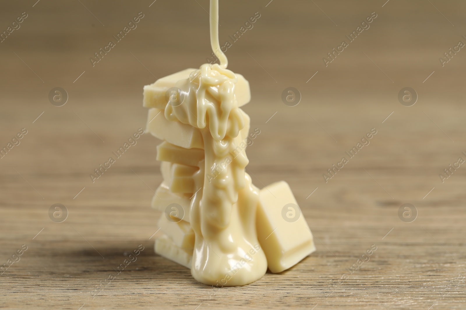 Photo of Pouring tasty white chocolate paste onto pieces on wooden table, closeup