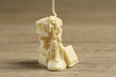 Pouring tasty white chocolate paste onto pieces on wooden table, closeup