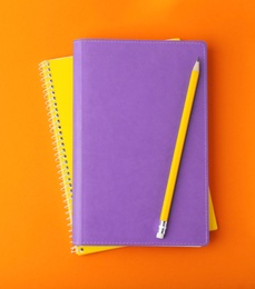 Photo of Notebooks with pencil on orange background, top view. Space for text