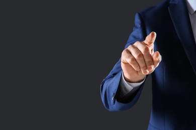 Businessman touching empty virtual screen against dark background, focus on hand