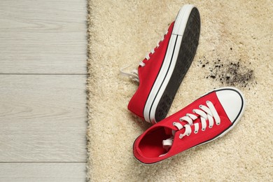 Photo of Red sneakers and mud on beige carpet, top view. Space for text