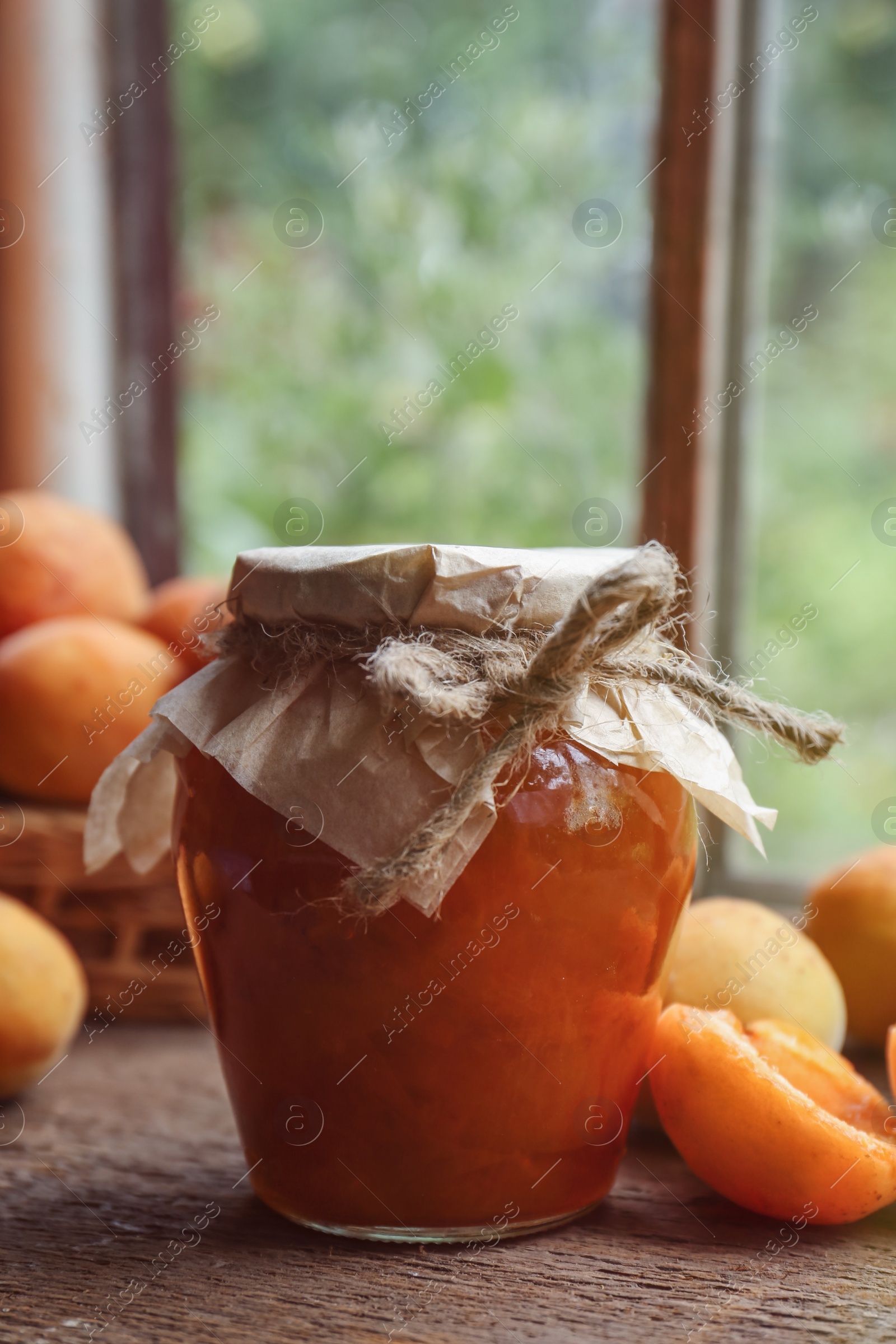 Photo of Jar of delicious jam and fresh ripe apricots on wooden table indoors. Fruit preserve