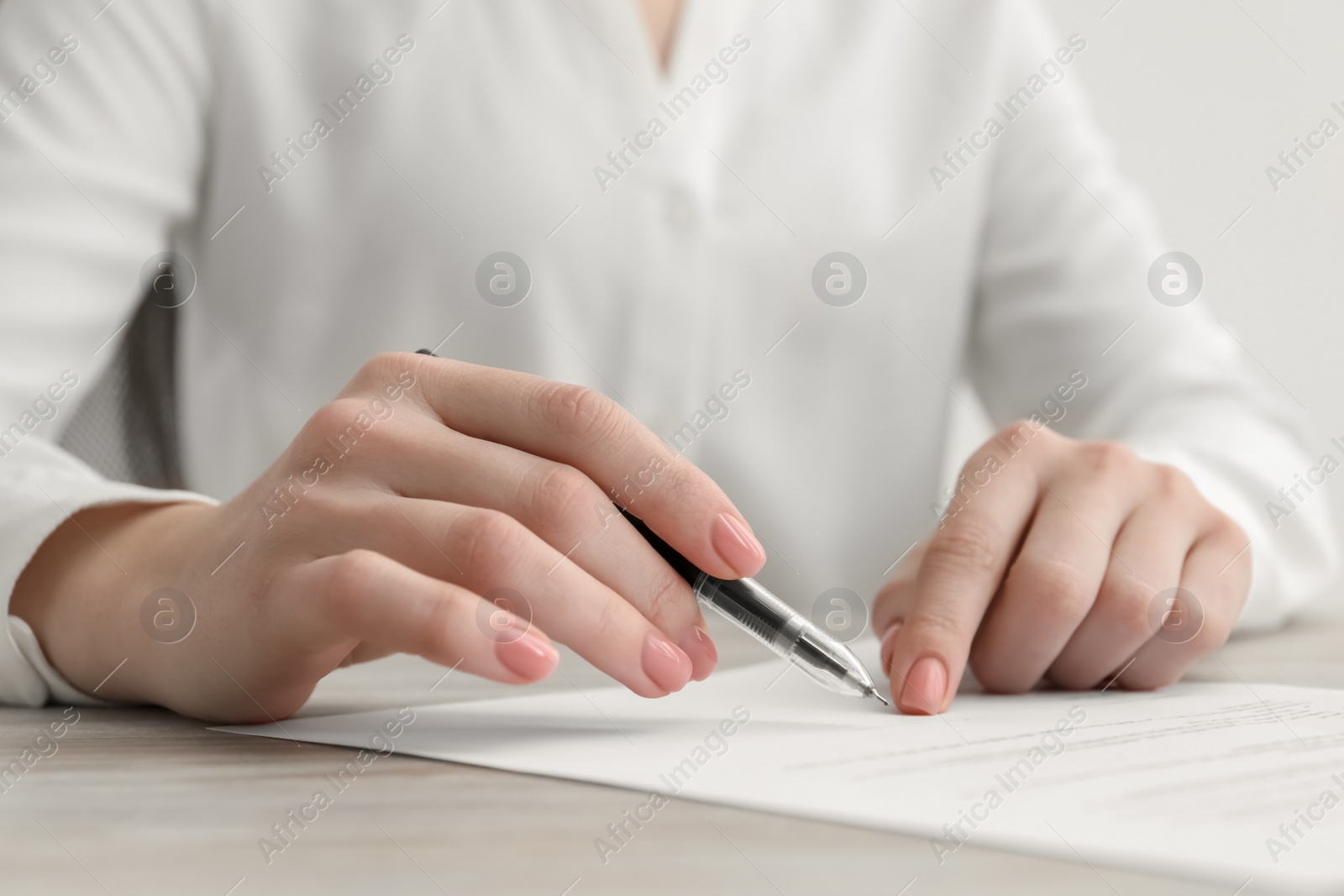 Photo of Woman signing documents at wooden table in office, closeup