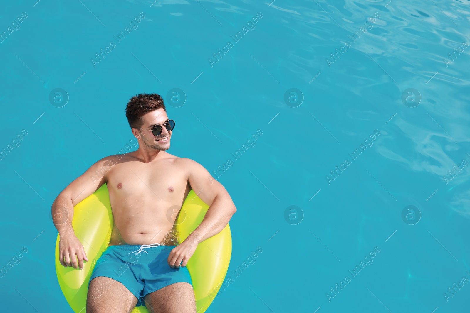 Photo of Handsome young man with inflatable ring in swimming pool on sunny day, above view. Space for text