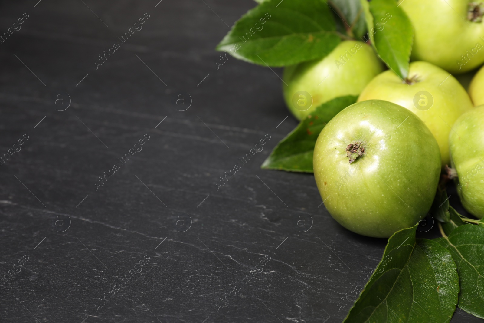 Photo of Ripe green apples with leaves on dark grey table, closeup. Space for text