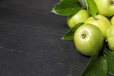 Photo of Ripe green apples with leaves on dark grey table, closeup. Space for text