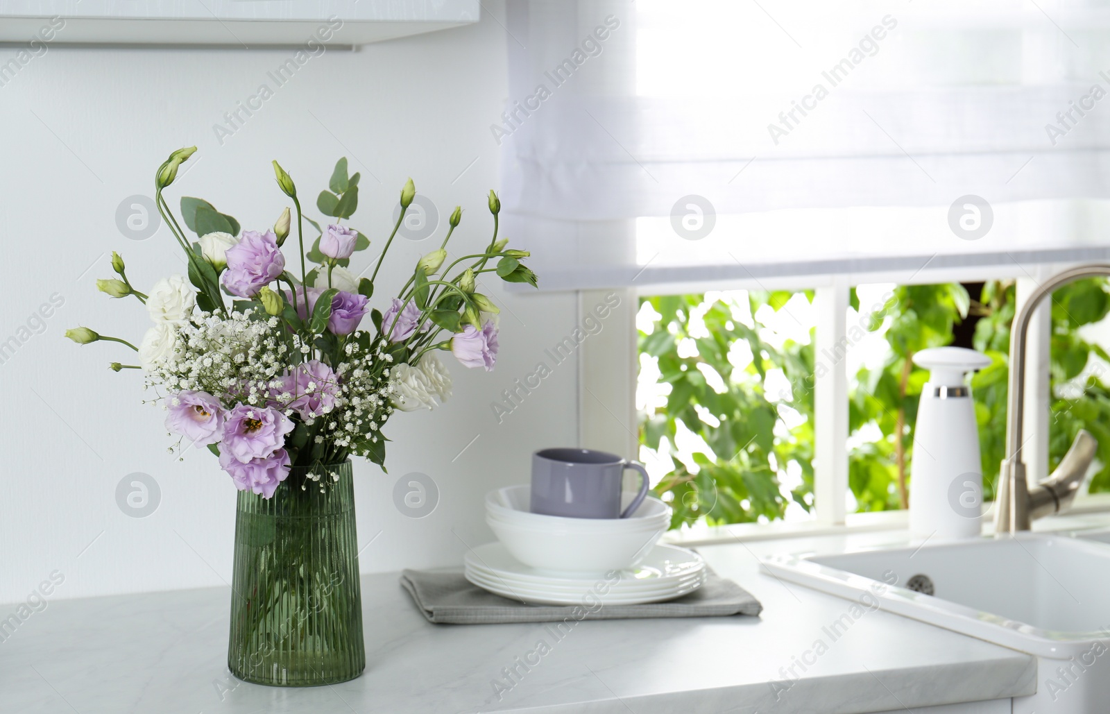 Photo of Beautiful bouquet with Eustoma flowers and dishware on countertop in kitchen. Space for text