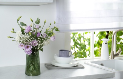 Photo of Beautiful bouquet with Eustoma flowers and dishware on countertop in kitchen. Space for text