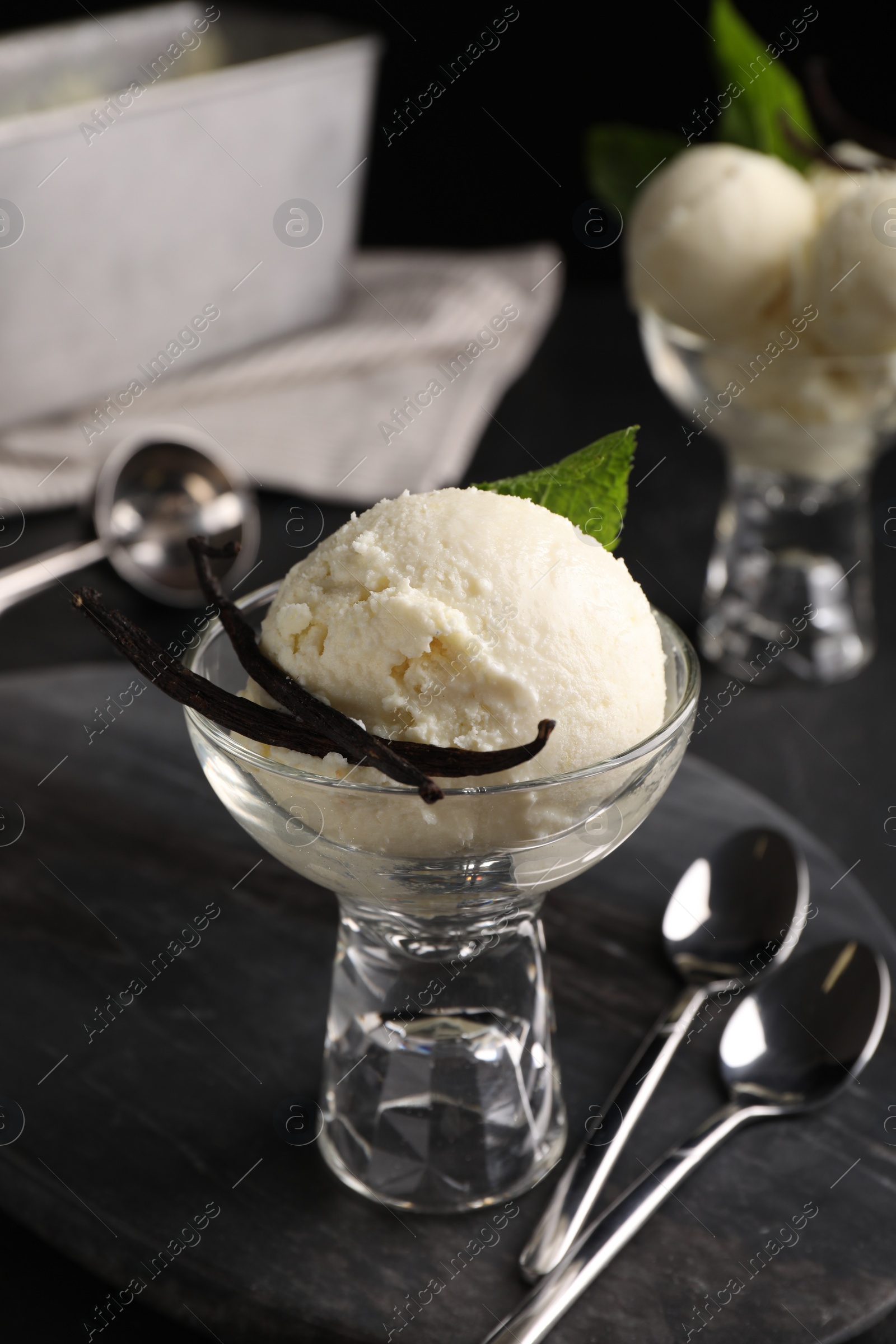 Photo of Tasty ice cream with vanilla pods in glass dessert bowl on black table