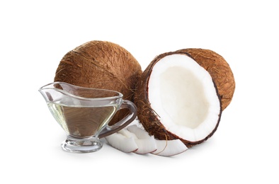 Photo of Ripe coconuts and gravy boat with natural organic oil on white background