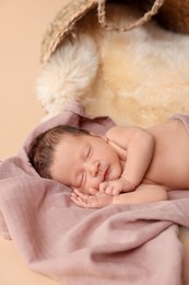 Adorable newborn baby sleeping on faux fur near overturned wicker basket against beige background
