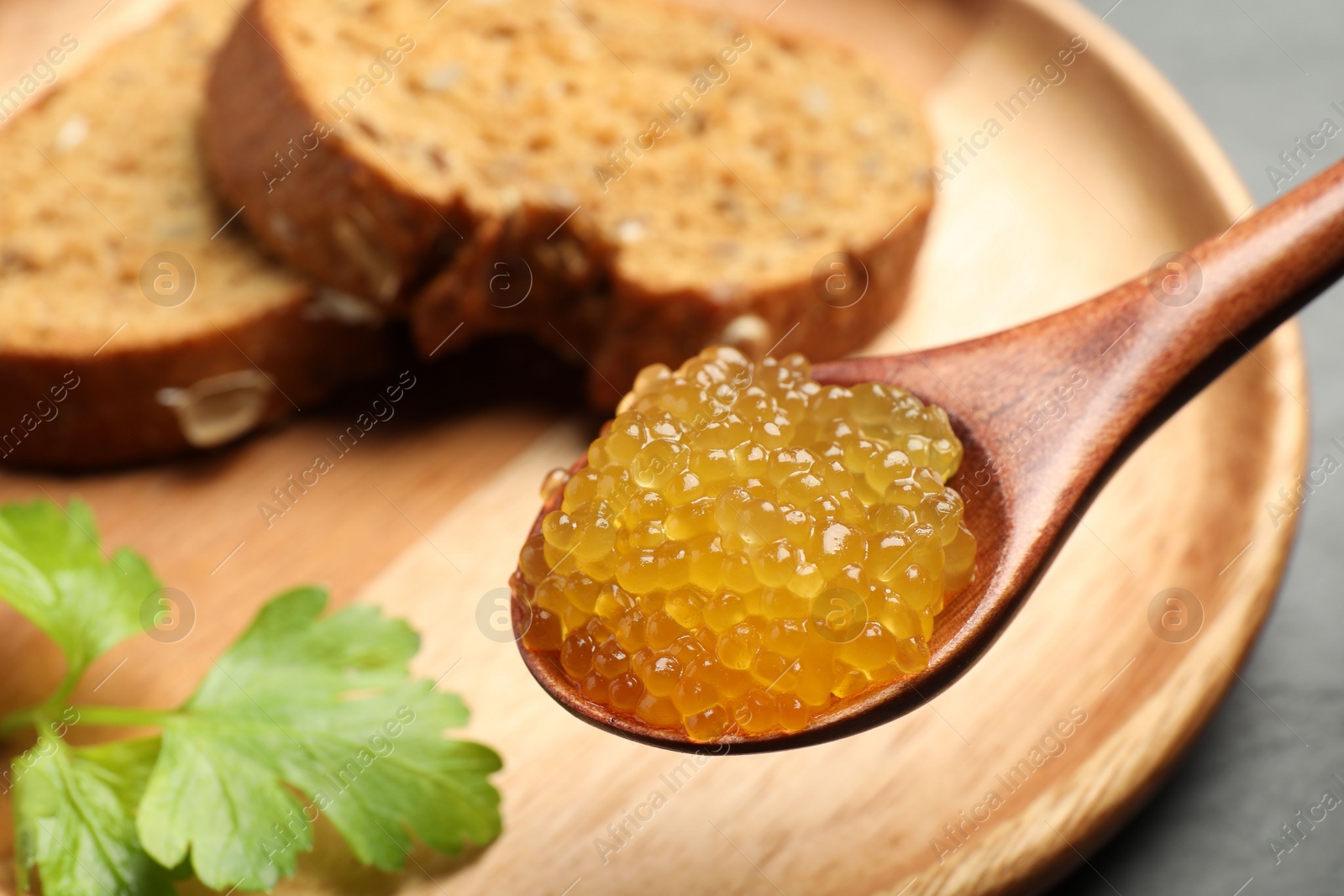 Photo of Fresh pike caviar in spoon, bread and parsley on grey table, closeup