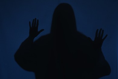 Silhouette of creepy ghost behind dark blue cloth