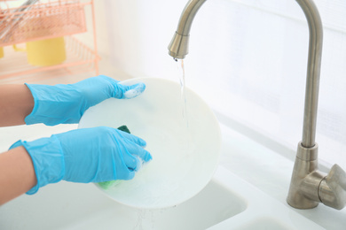 Photo of Woman washing ceramic plate in kitchen, closeup