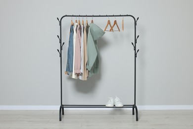 Photo of Rack with stylish clothes on wooden hangers and shoes near light grey wall