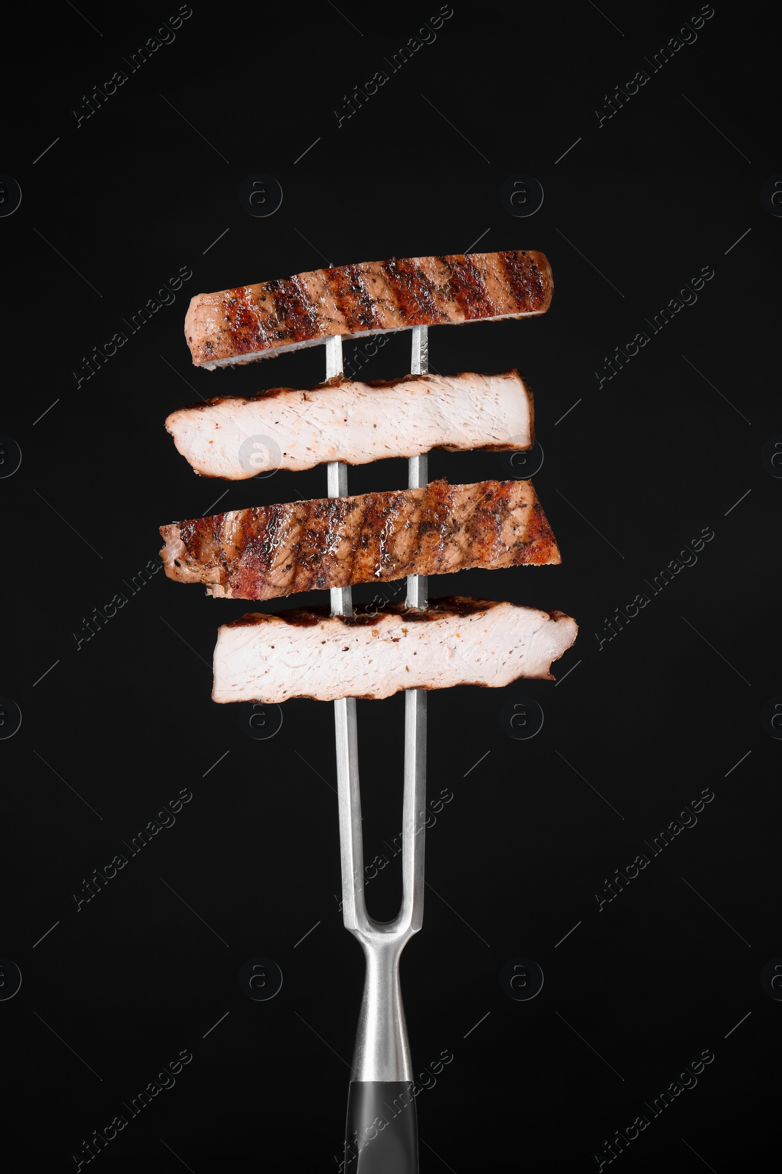 Photo of Carving fork with cut grilled pork steak pieces against black background