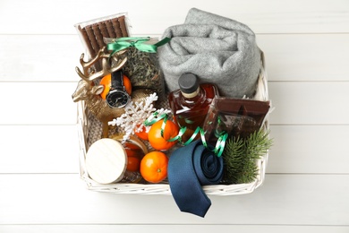 Wicker basket with Christmas gift set on white wooden table, top view