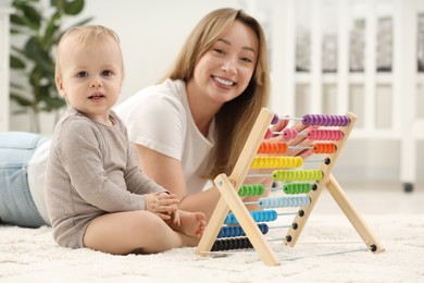 Children toys. Happy mother and her little son playing with wooden abacus on rug at home