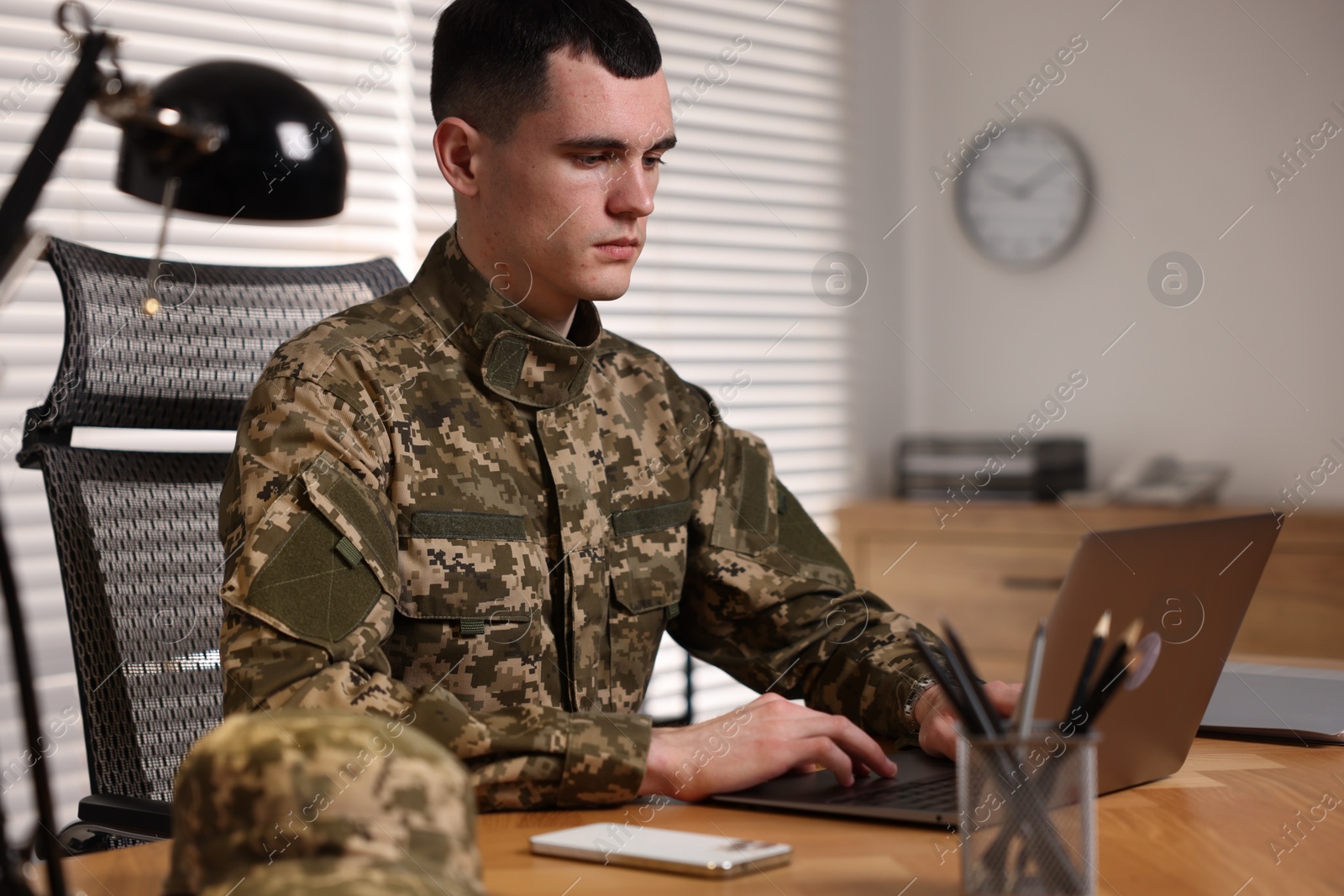 Photo of Military service. Young soldier working at wooden table in office