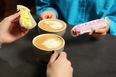 Photo of Young women with coffee and eclairs spending time together in cafe, closeup
