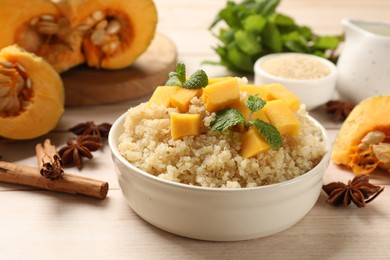 Photo of Tasty quinoa porridge with pumpkin, mint in bowl and spices on light wooden table