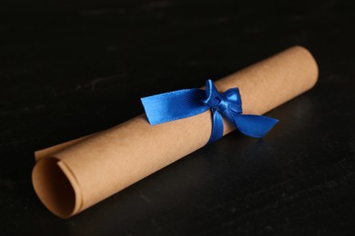 Photo of Rolled student's diploma with blue ribbon on black table