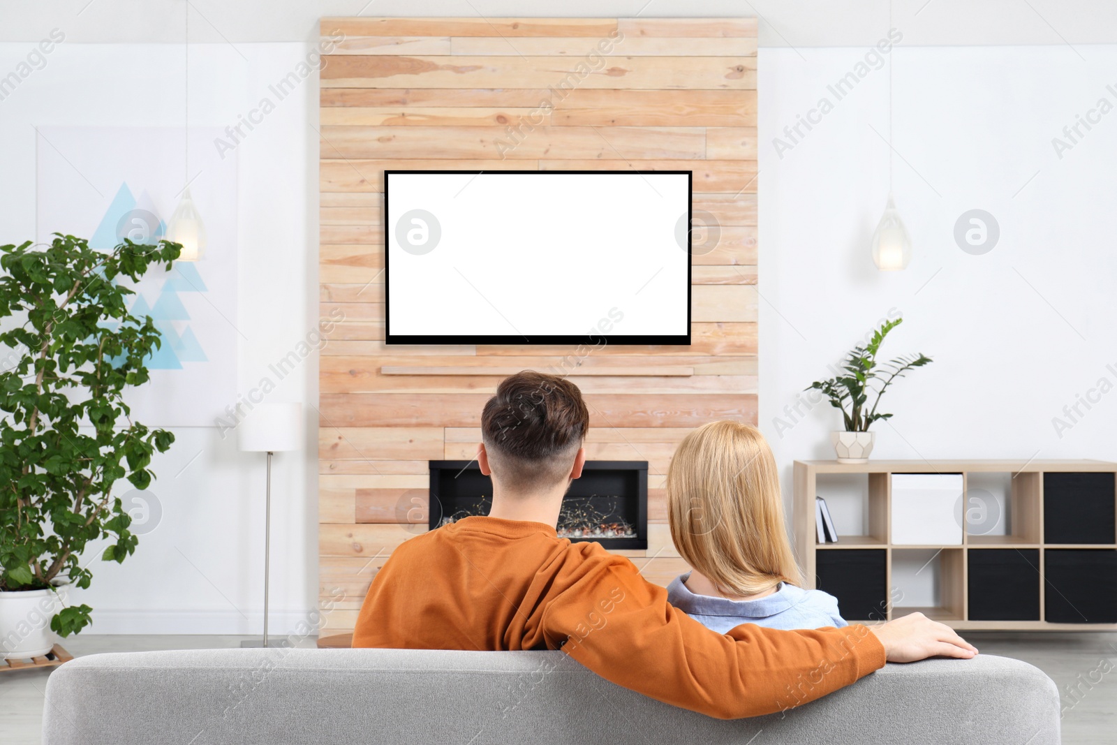 Photo of Couple watching TV on sofa in living room with decorative fireplace