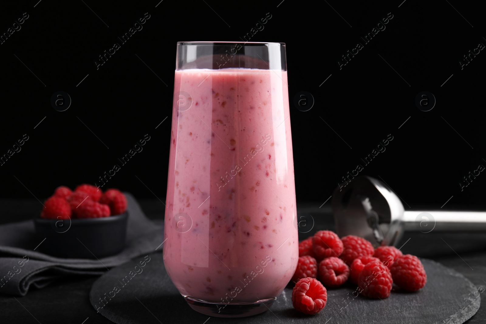 Photo of Glass of tasty raspberry smoothie on dark table against black background